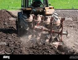 Heavy tractor with multi-disc plough working farmland for cassava production showing deep soil inversion for weed seed bank depletion