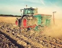 Tractor applying fertilizer to ploughed cassava farmland in West Africa to enhance soil nutrition before planting